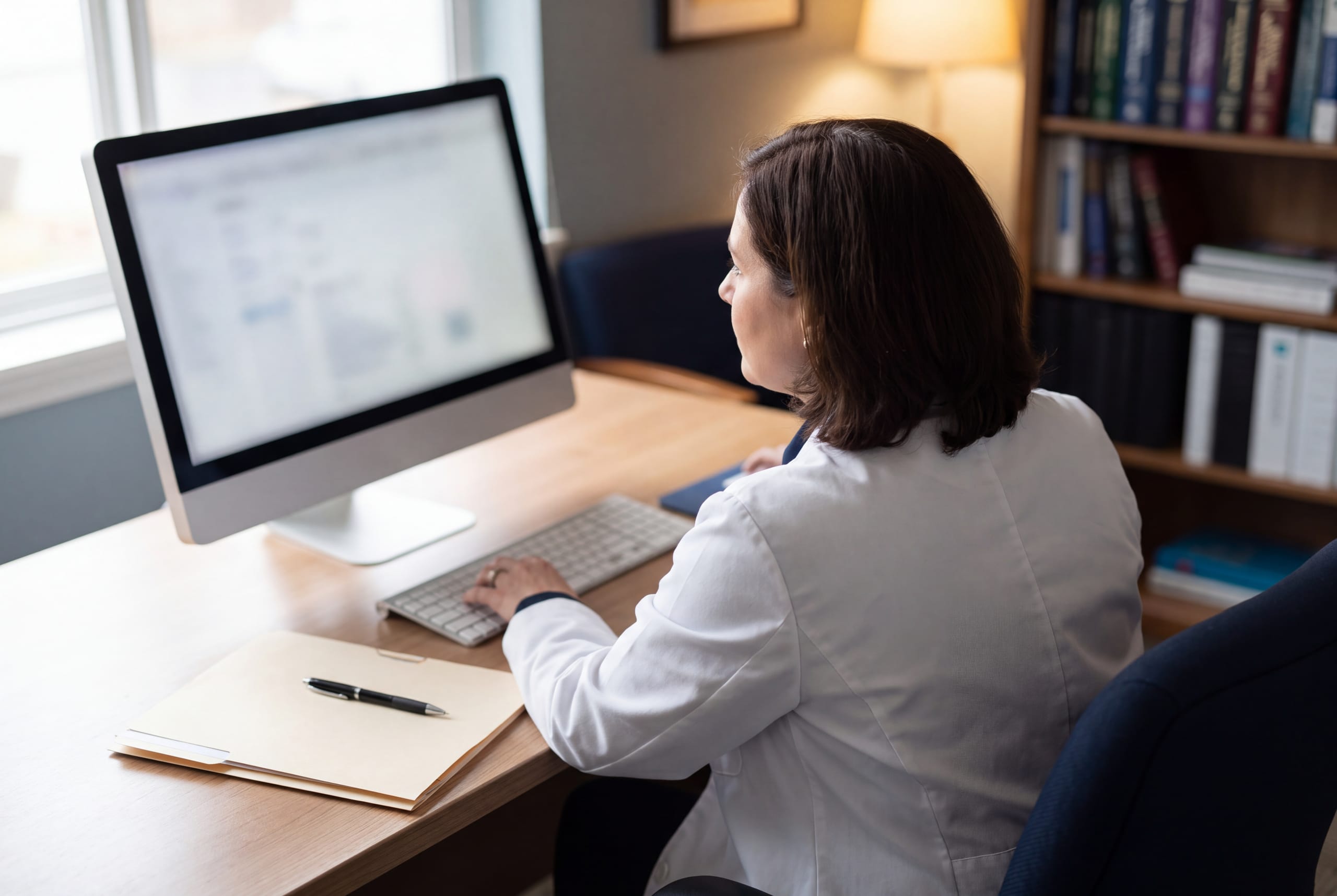 A consultant pathologist at a desk reviewing work on a monitor, seen from behind.